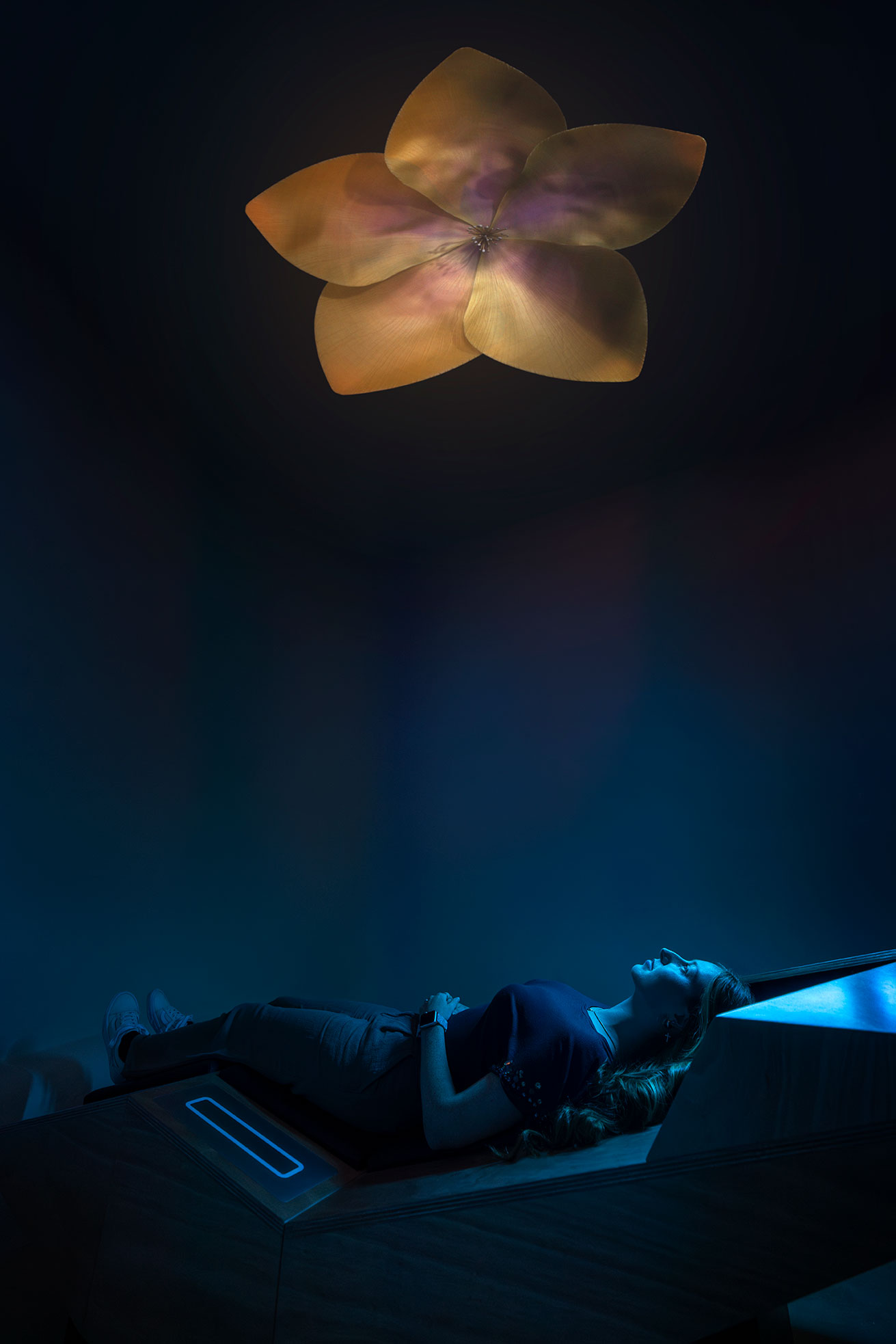 Woman lying on her back, looking up at a flower installation.